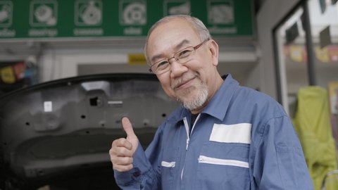 Asian elderly man are car mechanic Wear uniform, stand smiling, happy in service to customers. Professional Mechanic with factory work experience. Car maintenance business. Concept key worker