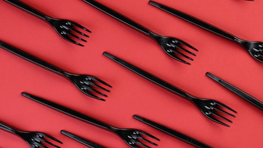 Eco concept. Plastic disposable forks stacked in rows on a red background rotate in a circle. Pattern