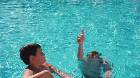Cheerful kids relaxing during summer vacation, teenage boy showing thumb up in the pool while diving