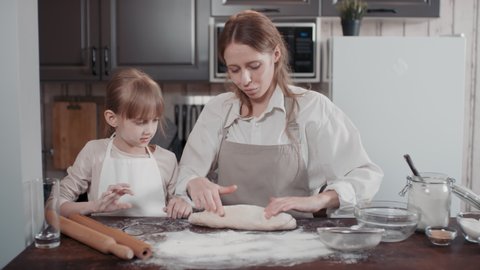 Waist-up footage of cheerful mom and daughter with faces smudged in flour cooking homemade bread creating bread shape from elastic smooth yeast dough talking and enjoying process