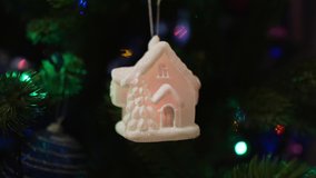 Christmas tree decoration in the form of a glowing fairy-tale snow-covered house in the light of colored garlands.