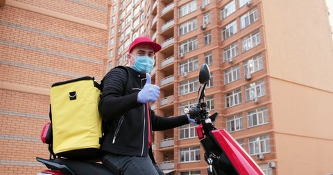 A delivery man with a yellow backpack, face mask and gloves appears in the video on an electric moped and shows a thumb up. Excellent delivery during quarantine.