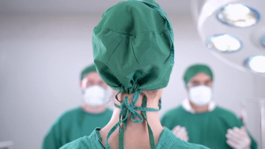 doctor woman smiling and taking off the medical face protection, while staff and doctor working in surgery room at medical facility. With lighting equipment in operation room hospital. Royalty-Free Stock Footage #1064580793