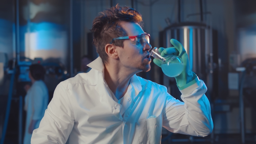 Mad scientist drinking blue liquid from glass flask in industrial lab. Portrait of crazy male professor in white coat, gloves and glasses drinking chemicals working in laboratory Royalty-Free Stock Footage #1064581285