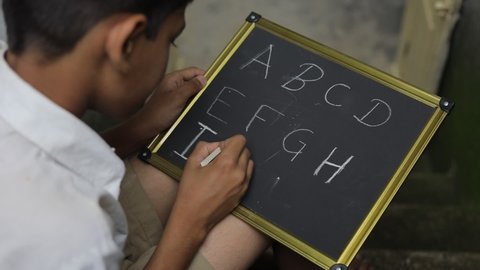 Indian child writing A B C D alphabet on Chalkboard