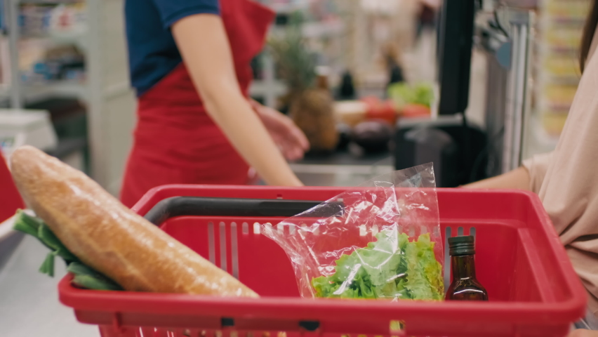Midsection footage of unrecognizable female customer placing healthy products in red product basket after being scanned by cashier in hypermarket Royalty-Free Stock Footage #1064587588