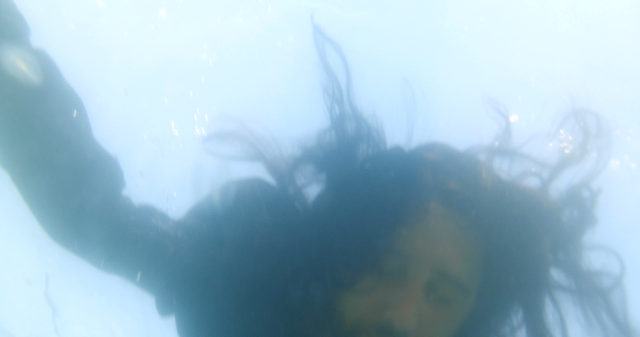 Close-up underwater shot of a long-haired man in black clothes lying in the water and drowned surrounded by jellyfish. The concept of lost hope and suicide. 4k slow motion