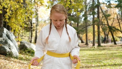 teenager girl 12 years old is engaged in karate outdoors in the park. Healthy lifestyle concept. playing sports. martial arts. Judo, Jiujitsu. bold, strong. ties a belt on a kimono