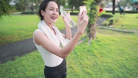Young asian female video calling with friends during exercising at the park, holding plastic water bottle, enjoy exercise sharing healthy life experiences, having online conversation, positive emotion
