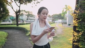 Young active Asian woman video calling with friends while exercising at the park with sunset on background, sharing healthy lifestyle stories, human modern technology, adaptation new normal distancing