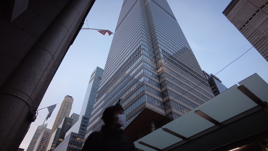 New York City, USA - Dec 24, 2020: Tall skyscraper office building on 42nd Street in Midtown with American USA flag and people walking with face masks in foreground. Low angle view with sky.  | Shutterstock HD Video #1064602435