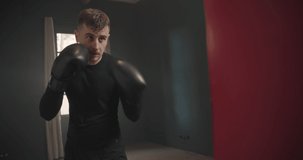 A young athletic man is hitting a boxing bag. Boxer practicing punches in the ring. The athlete strikes with a punching bag. 4k video