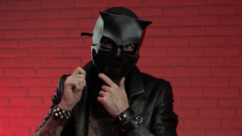 a man in a demon skull mask wearing a leather cloak with leather bracelets and straps on his body