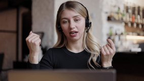 Happy young business woman wears headset talks to web camera making distance online video conference call. Female internet teacher doing distant chat working from coffee house. job interview.