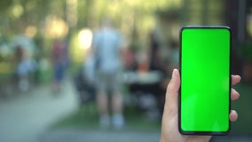 Close up hands woman holding phone with vertical green screen on busy street background pavement scrolling pages swiping surfing internet technology chroma key message