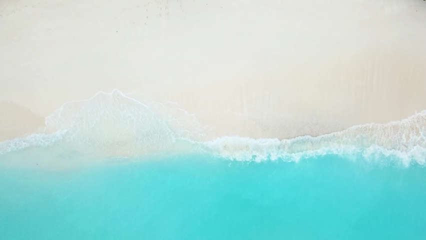 An aerial view of turquoise lagoon waves gently breaking on to the white sandy beach. | Shutterstock HD Video #1064615179