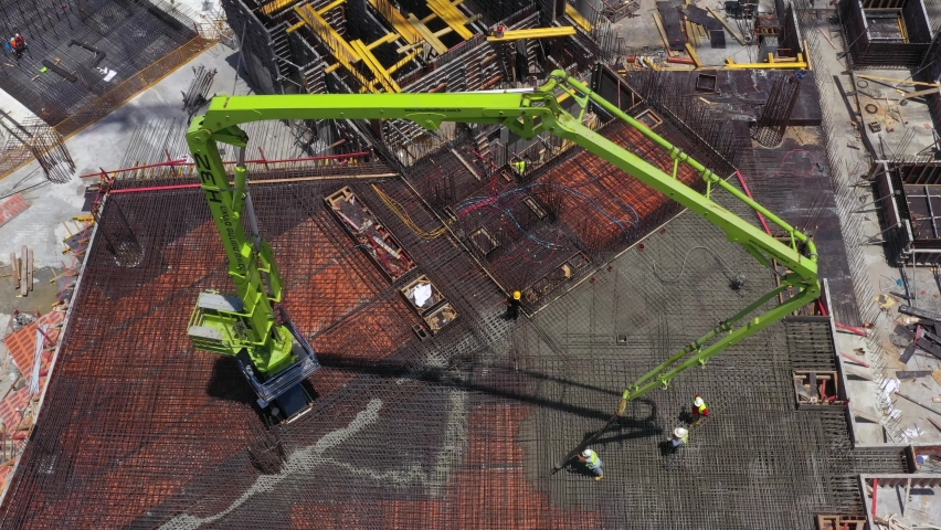 Tel Aviv, Israel - December 21, 2020: Concrete Pump operation in a large Construction site, with workers guiding and casting a new floor level, Aerial view. 