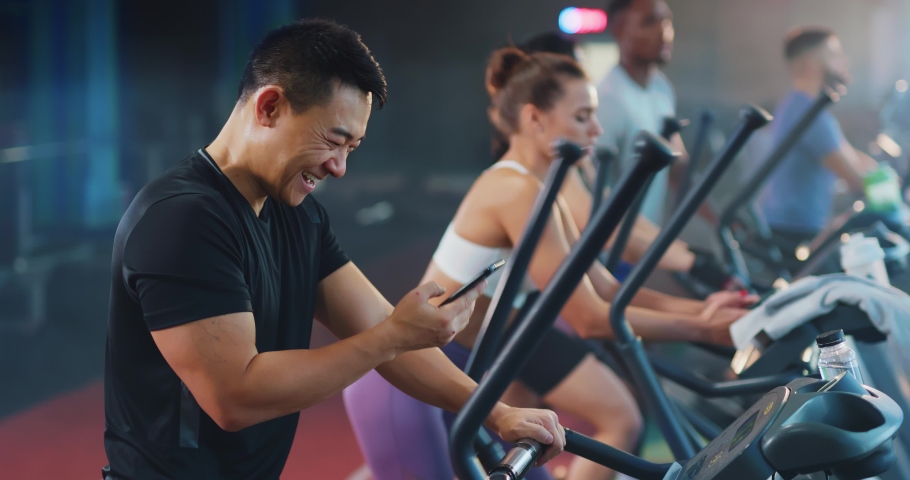 Asian handsome young positive man chatting messages using smartphone recording voice audio message while workingout with team sports in modern gym.