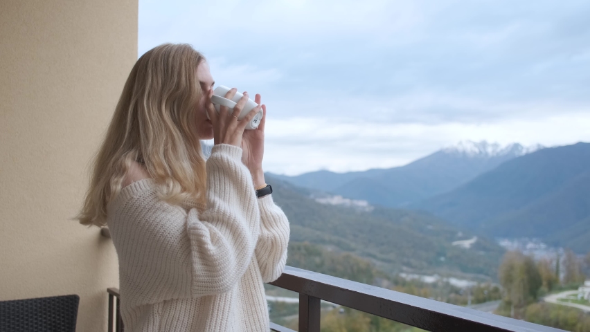 blonde woman drinking tea on the balcony overlooking the mountains