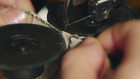 A tailor connects two leather parts on a furrier. Manufacturing of leather goods using professional equipment. Close-up