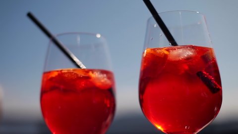 A glass of cocktail.Juicy delicious drink.red cocktail with ice with lemon slices in a glass with a straw on a background of blue sky