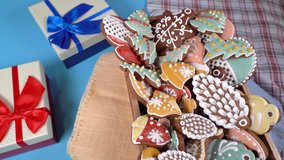 A dish of Christmas gingerbread with different shapes-snowflakes, firs, mittens, stars, sleigh, cones, bells rotates on the table, blue background. Festive decorations all around.
