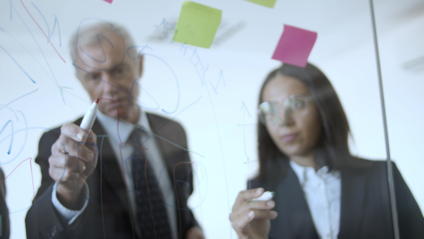 Group of managers working on project strategy, drawing charts on glass board with sticky notes. View through glass wall. Business plan concept | Shutterstock HD Video #1064632753
