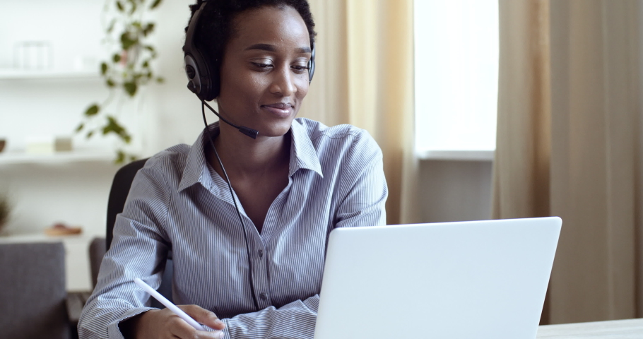 Young black girl with short hair foreign student learns language remotely listening in headphones teacher speaks with tutor on video conference watches lesson online in laptop makes notes in notebook | Shutterstock HD Video #1064635813