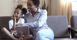 Young mother with her cute daughter looking in digital tablet mother teaches child african american girl uses computer graphic pad laugh together smile chuck tickle, modern technology device concept