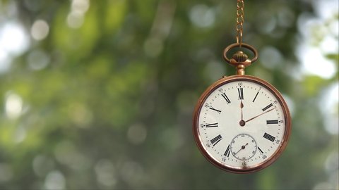 Pocket Watch on Chain Time is Ticking 4K loop features a gold pocket watch with hands spinning around and swinging back and forth with blurred leaves blowing in the wind in the background in a loop