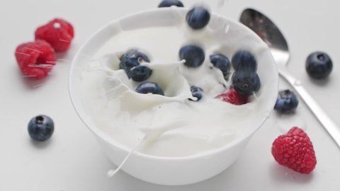 Fresh healthy food. Raspberries and blueberry falling into white bowl with yogurt and whipped cream. Fresh fruits in whipped cream. Organic berry, clean eating, vegan food concept. Slow motion.