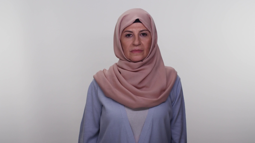 Beautiful old woman in an unhappy turban on a white background is making a suicidal gesture and imitating a gun with her hand. Slow motion video.