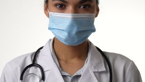 Receive care. Close up of attractive young female doctor wearing medical mask looking at camera, posing isolated on white background. Healthcare and medicine concept. Camera is moving up, slow motion