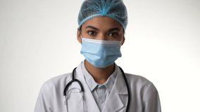 Professional. Attractive young female doctor with stethoscope taking off her medical mask isolated over white background. Healthcare and medicine concept. Slow motion