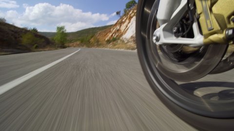 Motorcycle riding on a road in nature. Close up wheel on a bumpy asphalt road.