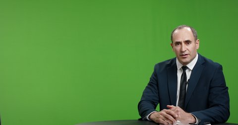 Male newsanchor informing about current news. Serious professional tv channel broadcast reporter pointing at graphics on green background 4k footage