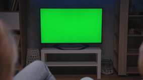 Family Couple Watches Green Screen TV Mockup Sitting on Couch in Living Room Together. Rear View on Casual People who Watching TV Green Screen in Domestic Cinema. Looking TV Show or News in Home Rest