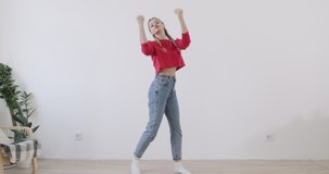 Girl recording dance moves at camera in front of white wall background. Young trendy woman dancing at home. Social media concept