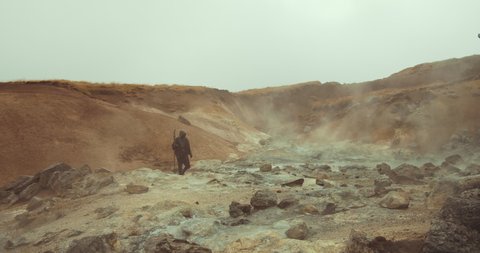 Slow Motion Handheld Wide Shot Of Mysterious Hooded Man In Robes Carrying Staff Through Misty Desert Landscape