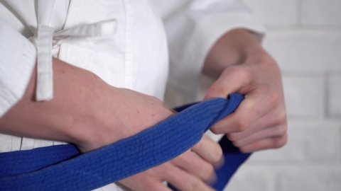 
a man in a white kimono ties a blue belt around his waist. The younger man is practicing seido karate