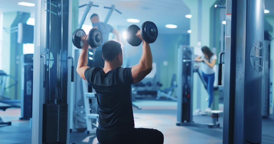 Active bodybuilder young asian man lifting heavy weights black dumbbells concentrating working out alone. Gym concept. Healthy lifestyle. | Shutterstock HD Video #1064679175