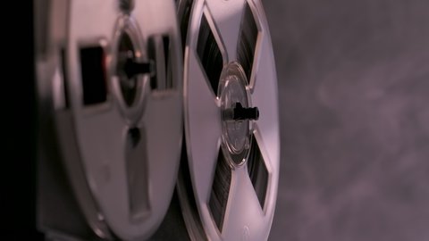 Audio reel to reel tape recorder, analog audio storage device. Tape deck plays music on dark background smoky studio with backlight. Monochrome. Spinning reels transparent close up. Slow motion.