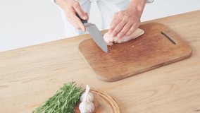 Cropped view of chef cutting chicken fillet near ingredients on table on white