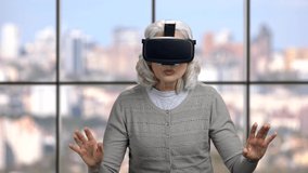 Mature woman wearing virtual reality headset. Senior woman using vr glasses on windows background. Modern technology concept.