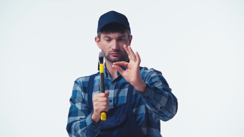 focused plumber in uniform and cap working with hammer isolated on white