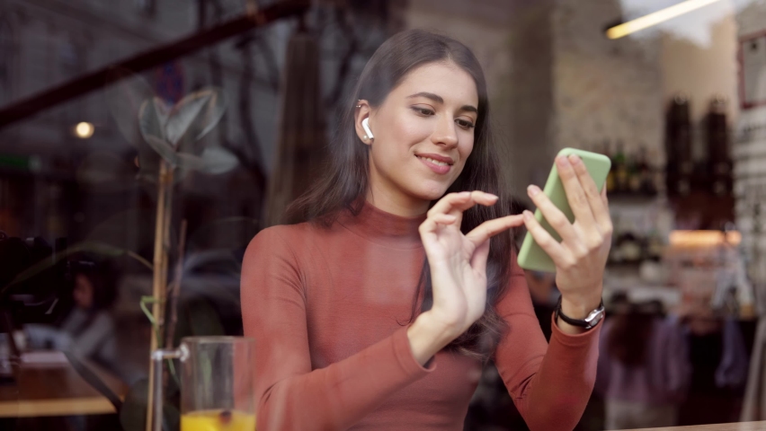 Young beautiful woman using mobile phone apps, texting message, browsing internet, watching video,tapping,looking at smartphone sitting in cafe. Studying online, remote working, courses online.