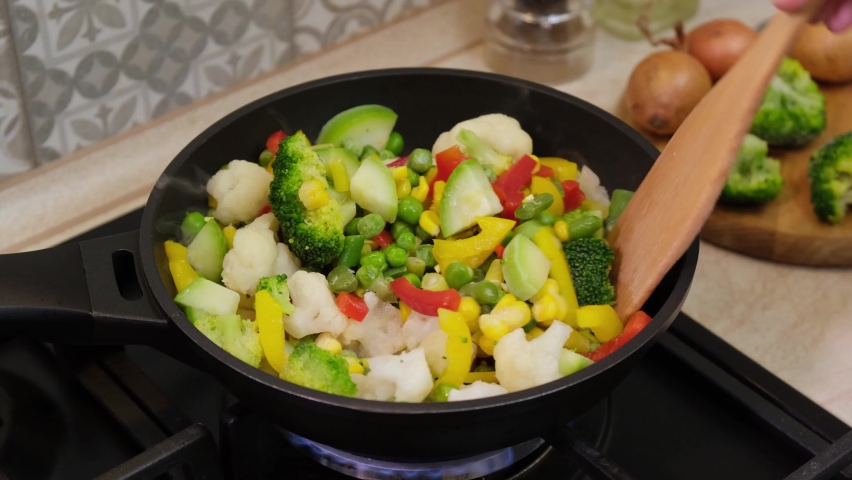 Cooking of frozen vegetables in frying pan. Frozen vegetables frying on hot pan. Natural food ingredients for healthy eating. Semi-finished food.
