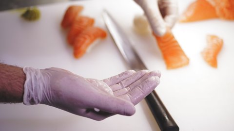 Traditional Japanese food. Sushi preparation. close-up. Sushi Chef, in disposable gloves, is preparing sushi with salmon and wasabi, on a backdrop of white cutting board at sushi bar. Japanese cuisine