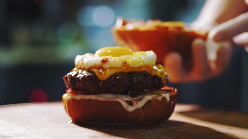 Cooking burgers. Close-up. Big appetizing burger with fresh cucumbers, tomatoes, juicy, grilled beef patty with cheese, and fried egg on top. fast food, junk food. | Shutterstock HD Video #1064691109