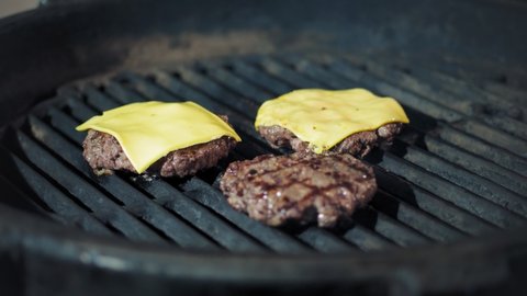 cookery. cooking burgers. Close-up. the chef turns over beef meat medallion, tossing it up. grilling of fresh meat burger patties with yellow melted cheese on brazier, hot flame barbecue grill, in